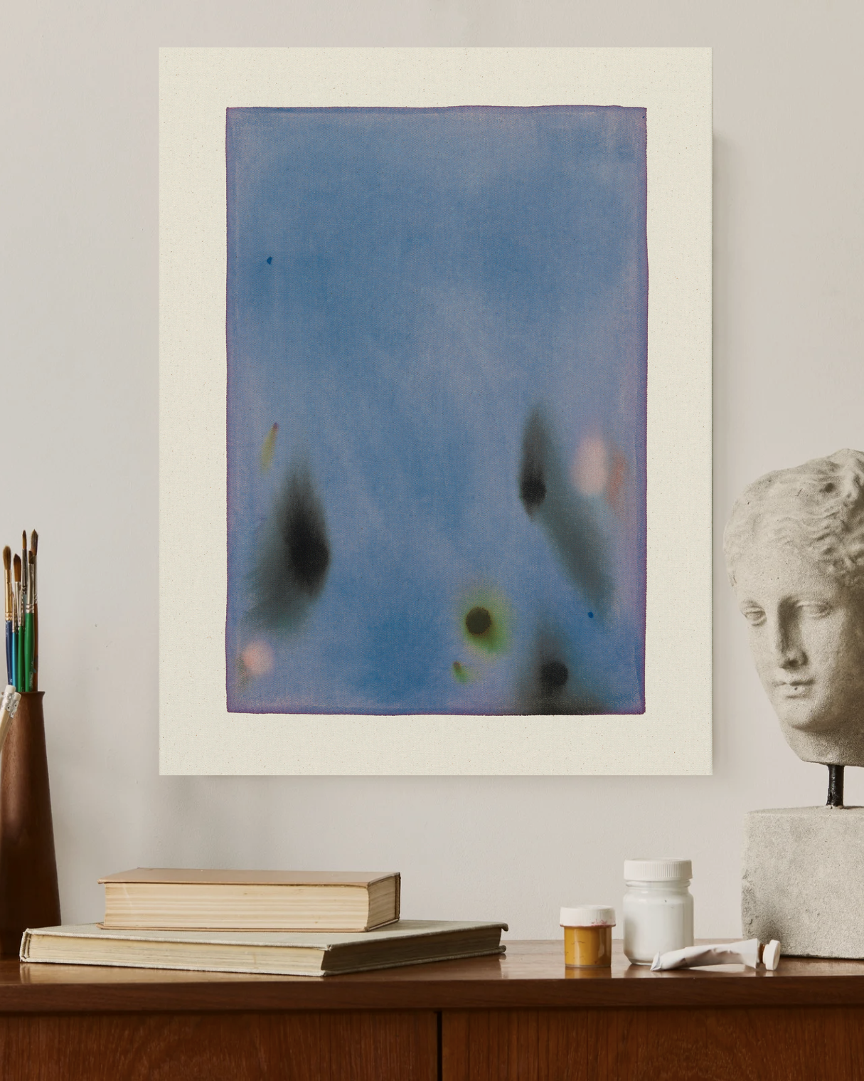 Abstract artwork on a wall with books and a statue in the foreground
